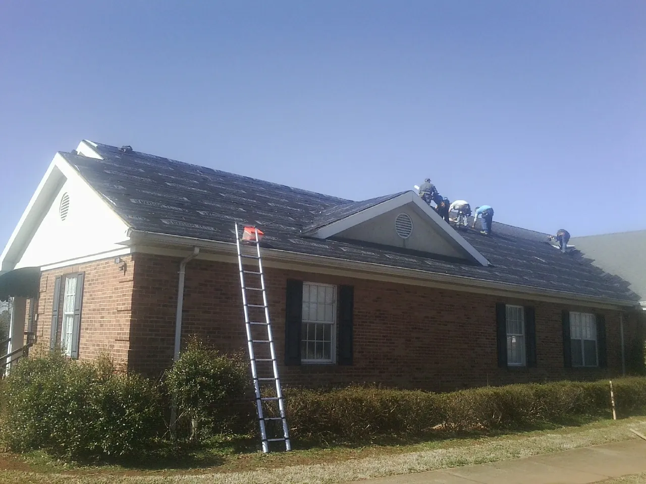 Crew tearing shingles off a brick ranch roof with a ladder set — Emergency Roof Repair work by our crew in Laguna Woods