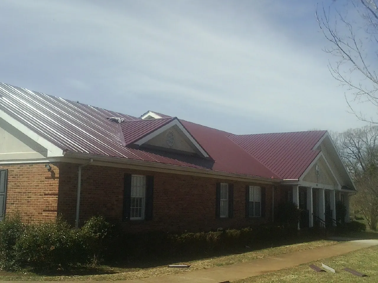 Red metal roof with gabled entries on a long brick building, from a Hail Damage Roof Repair job in Laguna Woods