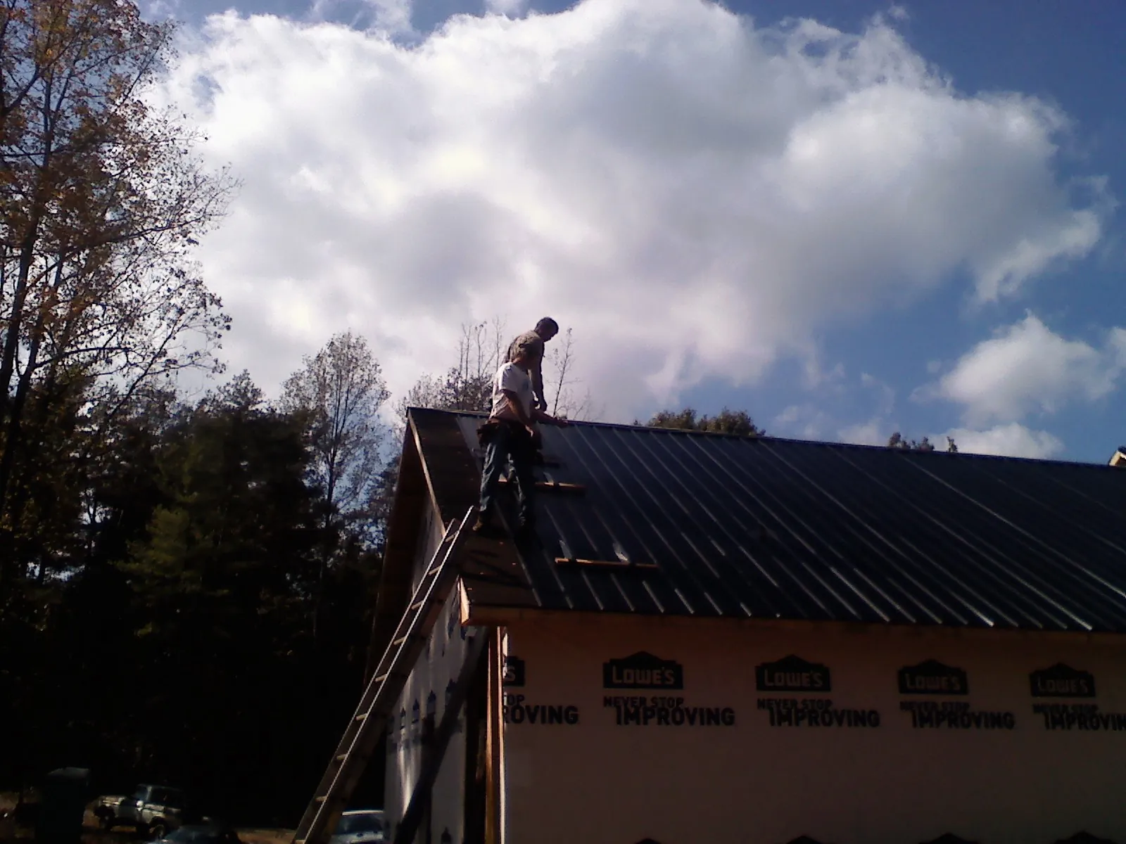 Roofer fastening dark metal panels high against a cloudy sky, from a Roof Inspection job in Laguna Woods
