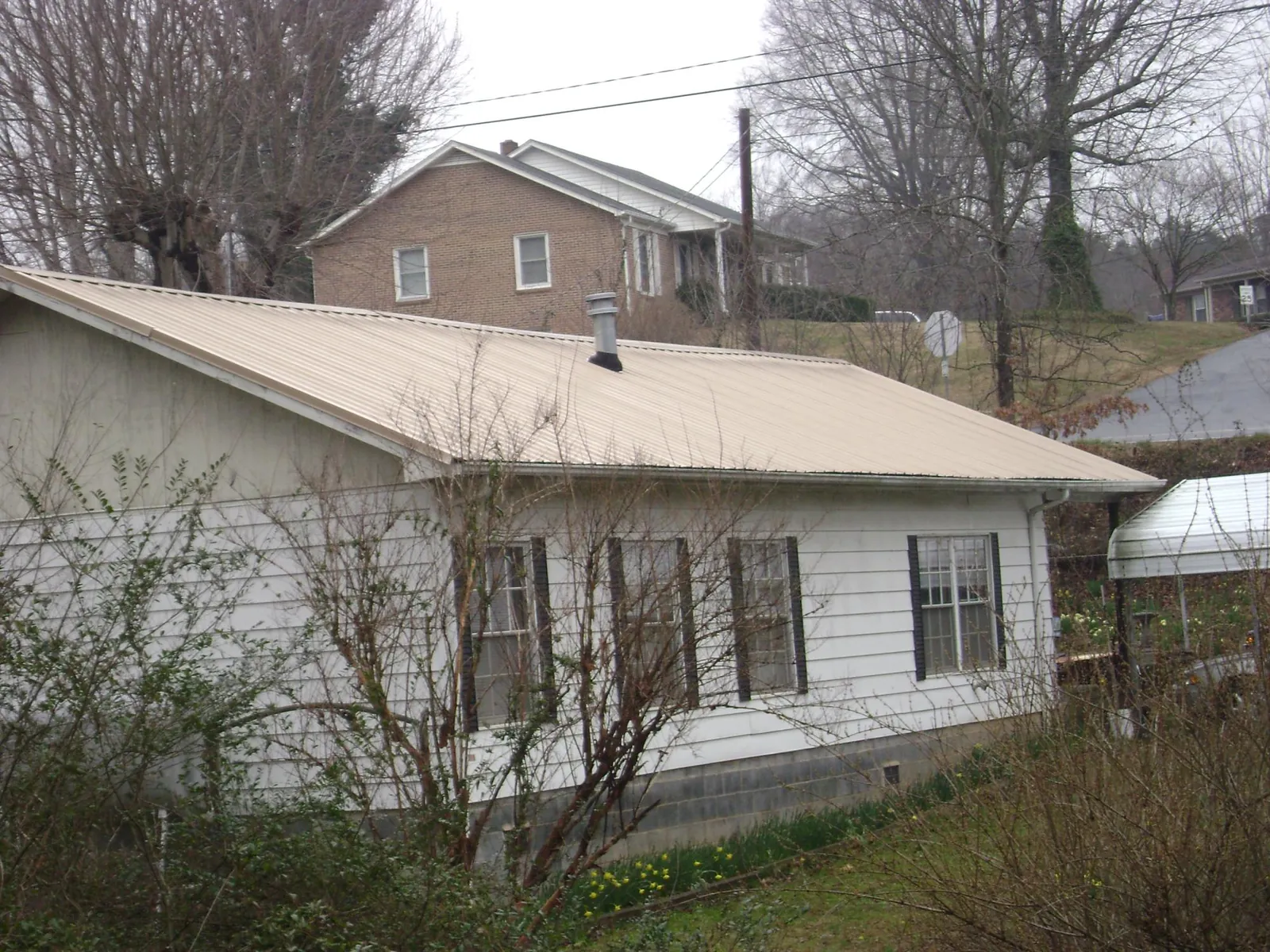 Tan metal roof on a white sided house set into a hillside — Commercial Roofing by Roofing Brothers in Laguna Woods